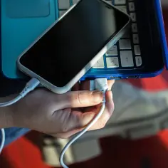 Dłoń podłącza kabel USB od telefonu do laptopa. Prosty sposób, jak połączyć telefon z laptopem, by przesłać dane lub naładować urządzenie.