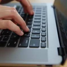 Dłonie piszą na klawiaturze laptopa. Dowiedz się, jak odblokować klawiaturę w laptopie, gdy przestanie odpowiadać.