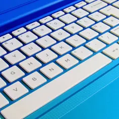 Klawiatura laptopa w kolorze niebieskim. Widoczne klawisze numeryczne i literowe. Dowiedz się, jak rozjaśnić ekran w laptopie, szukając odpowiednich skrótów klawiszowych.
