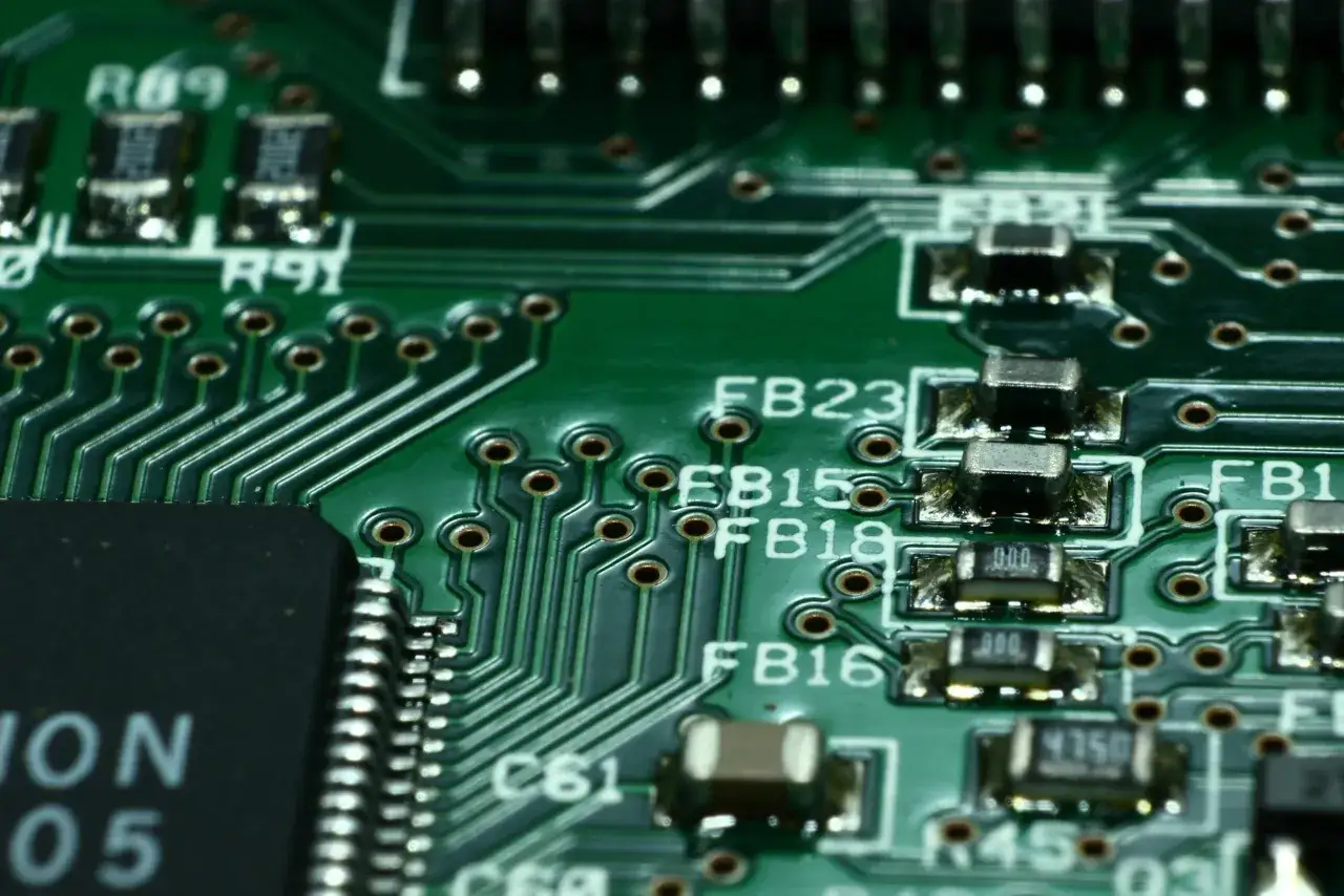 Zbliżenie na zieloną płytkę drukowaną z widocznymi elementami elektronicznymi, w tym kondensatorami i ścieżkami.
